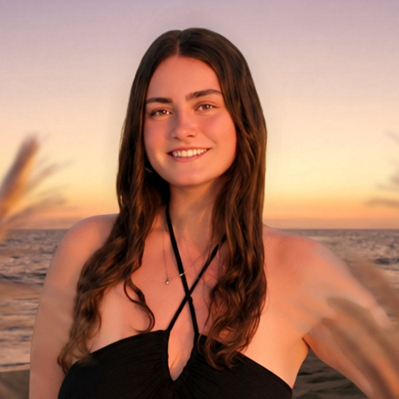 Woman in a black dress standing on a beach at sunset